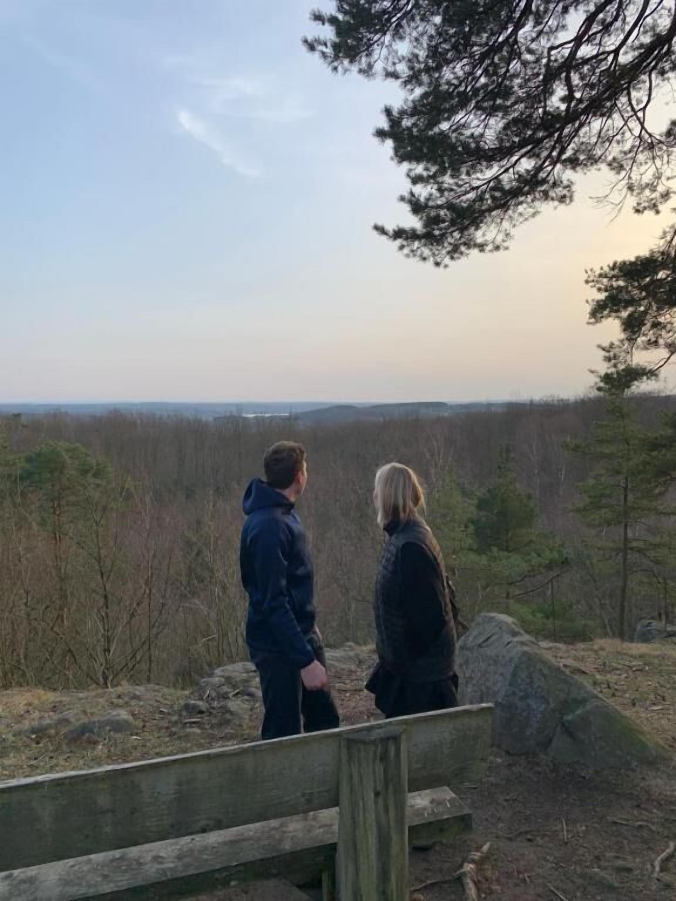 Dos personas en una plataforma de madera contemplando un paisaje boscoso.