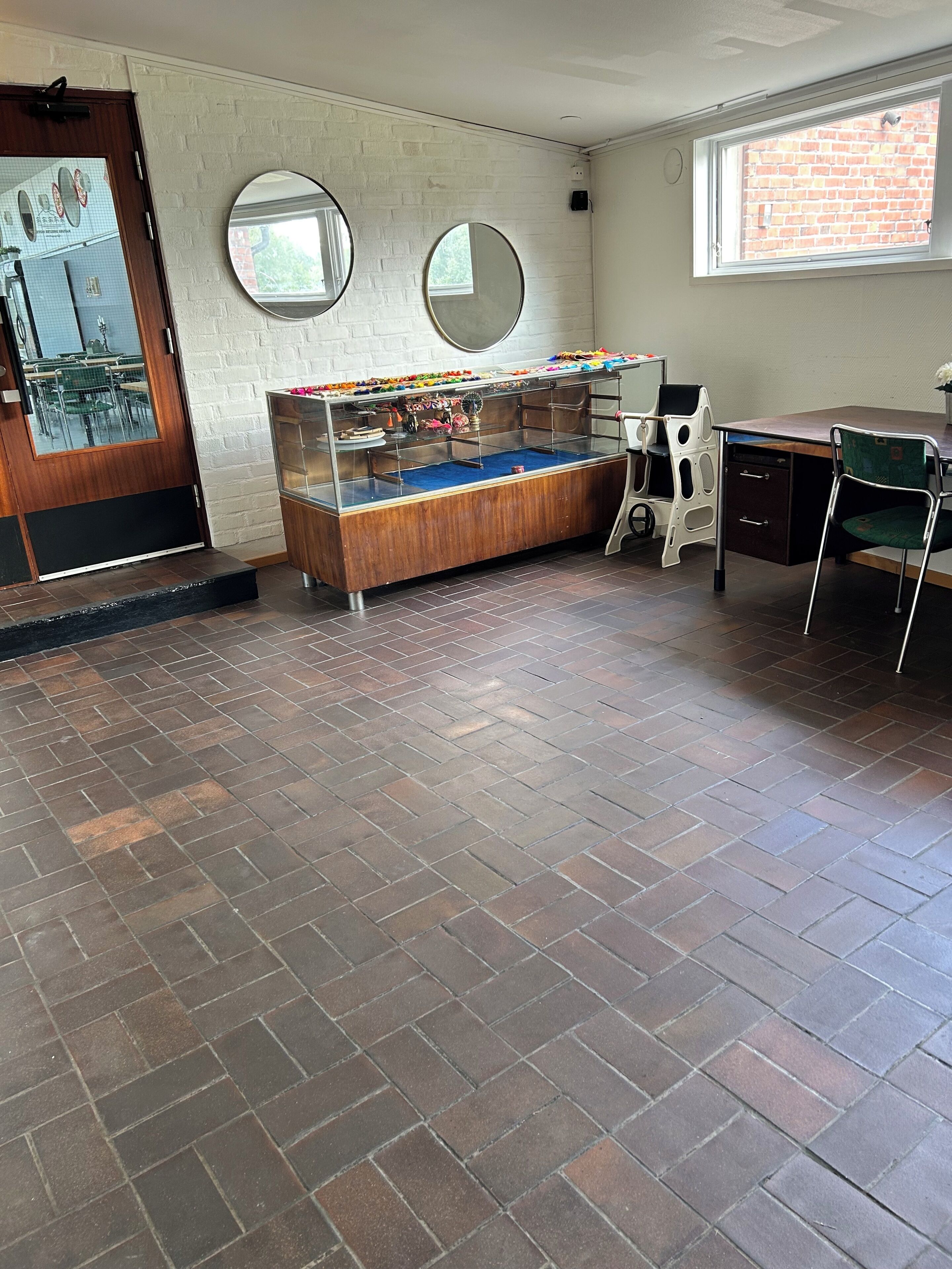 A room with a brick floor, a wooden door, a window, and a counter with a display.