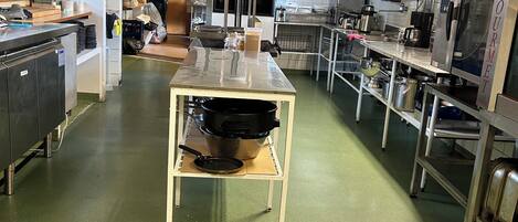 Ett rymligt professionellt kök med rostfria köksmaskiner, en central köksö och kakel på väggen bakom arbetsbänken.