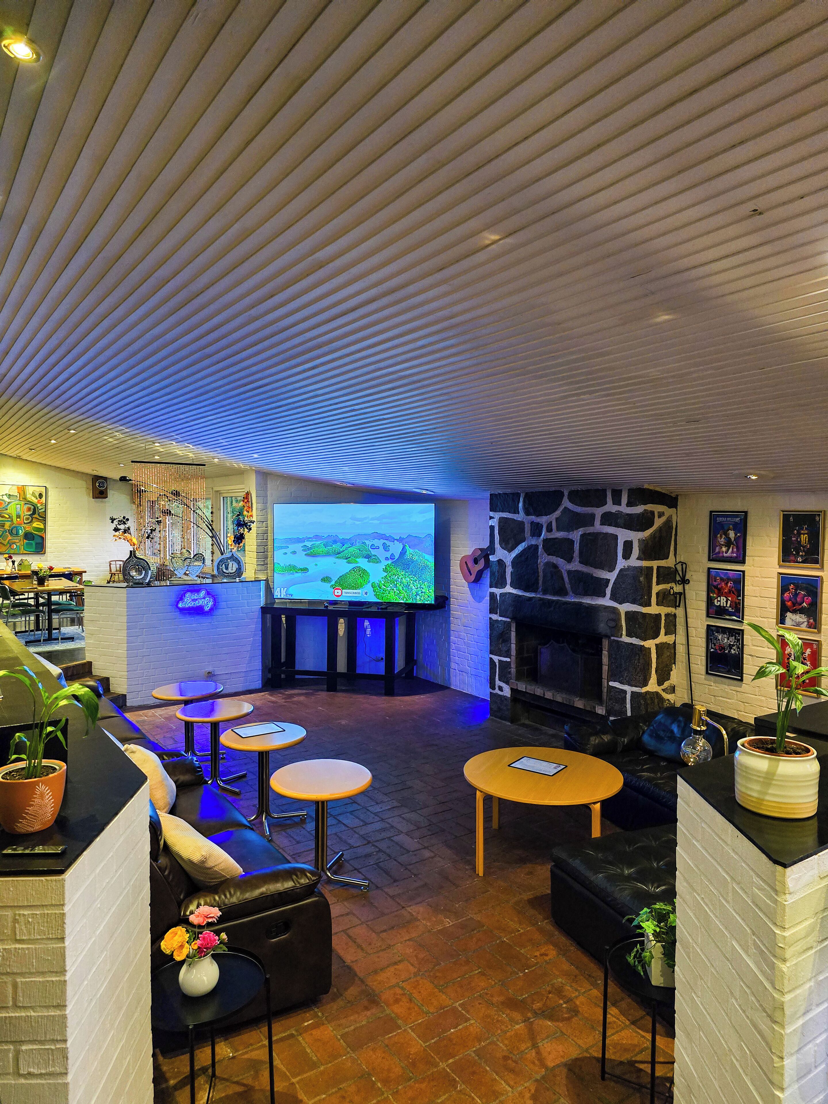 Ett mysigt loungeområde med en platt-TV, bekväma sittplatser, en öppen spis i sten och en bardisk med en neonreklamskylt.