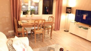 A cozy living room with a dining area, wooden furniture, a flat-screen TV, and a window with curtains. - Cozy apartment in the city center close to nature and main attractions (Savonlinna)
