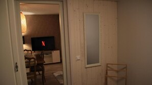 A room with a wooden floor, a bed, a TV displaying the Netflix logo, a dining table with chairs, and a mirror on the wall. - Cozy apartment in the city center close to nature and main attractions (Savonlinna)