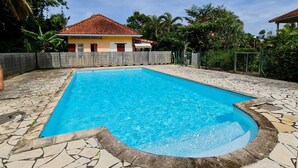 Una piscina rettangolare con bordi in pietra, circondata da una recinzione in legno e vegetazione rigogliosa.