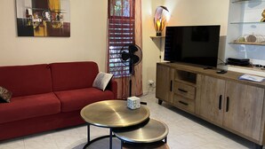 Un soggiorno con un divano rosso, una TV, un mobiletto in legno e un tavolino con un oggetto decorativo.