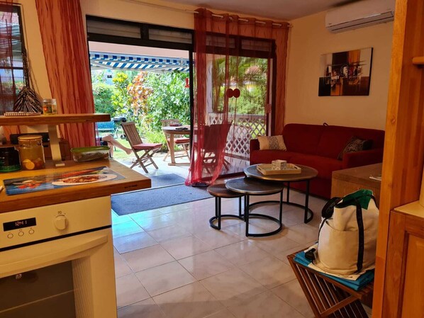 A cozy living area with a red sofa, two round tables, and a kitchen area with a stove and a clock.