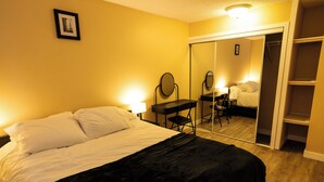 Hotellihuone, jossa on sänky, työpöytä tuolilla, peili ja vaatekaappi.