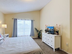 Een slaapkamer met een bed, een dressoir, een televisie en een raam met gordijnen.