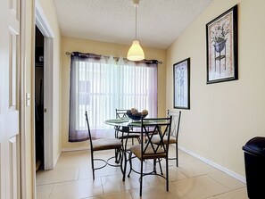 Comedor con una mesa, sillas, lámpara colgante y ventana con cortinas.