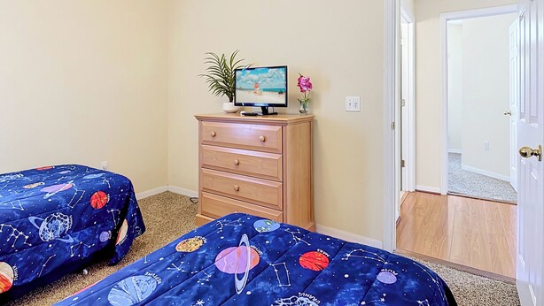 Een slaapkamer met twee bedden, een dressoir, een televisie en een deur naar een andere kamer.
