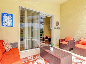 A poolside area with wicker furniture, a glass door leading to the pool, and a sign indicating pool towels. - Dream Weaver Villa® - Blooming Alamanda: Lakefront, Pool, Spa, Near Disney (Kissimmee)
