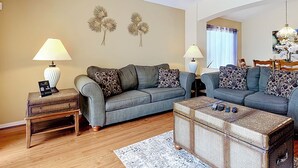 Een woonkamer met twee grijze banken, een bijzettafeltje, een rieten salontafel en een plafondventilator.