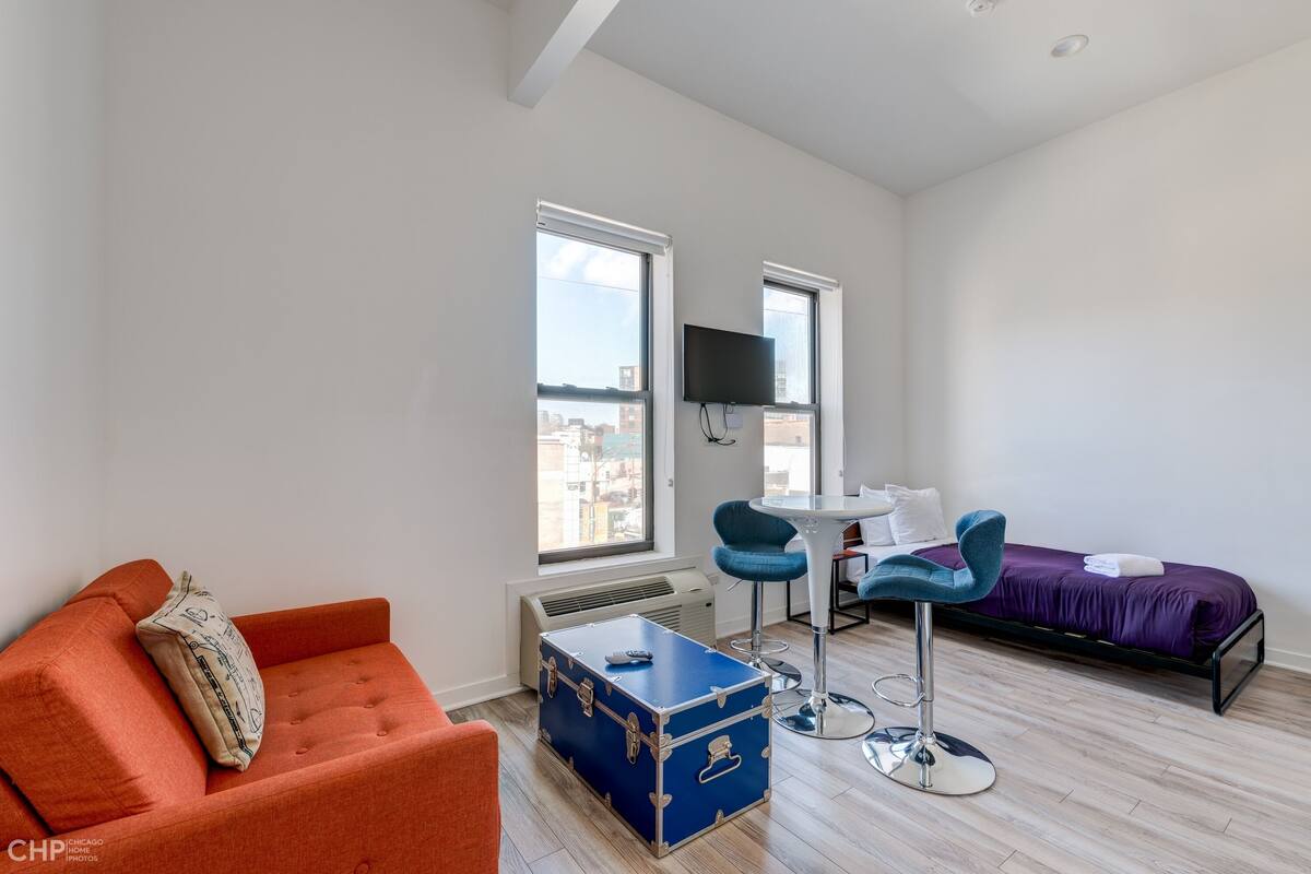 A modern, well-lit room with a sofa, a small table, a bed, and a large window.
