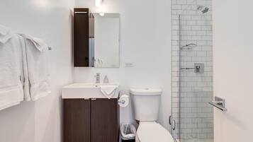 Une salle de bain moderne avec un lavabo blanc, un meuble en bois foncé, des toilettes blanches et une cabine de douche en verre.