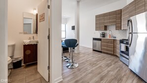 A modern kitchen with wooden cabinets, stainless steel appliances, and a bar stool. - Chicago Third Floor Studio by 747 Lofts (Chicago)