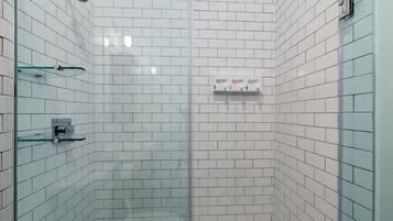 Ducha en esquina con azulejos blancos, estante de vidrio y panel de control.