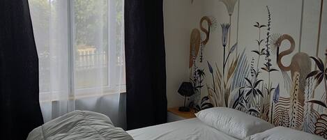 A bedroom with a bed, a nightstand, a lamp, and a wall with a floral mural.