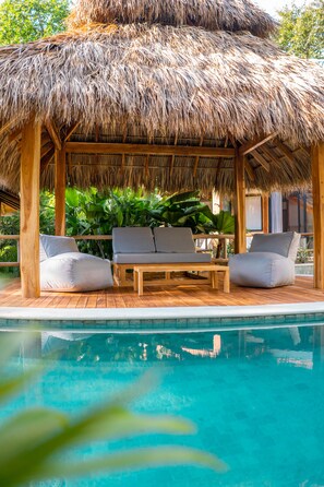 A poolside area with a thatched roof structure, wooden deck, and seating. - Blue Mist Hotel & Beach Club (Cóbano)