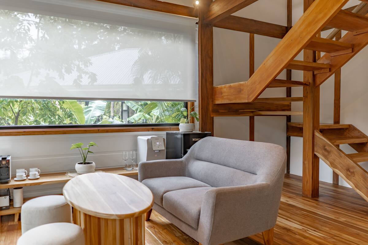A modern living room with a grey sofa, wooden floor, a small round table, a coffee machine, and a potted plant.