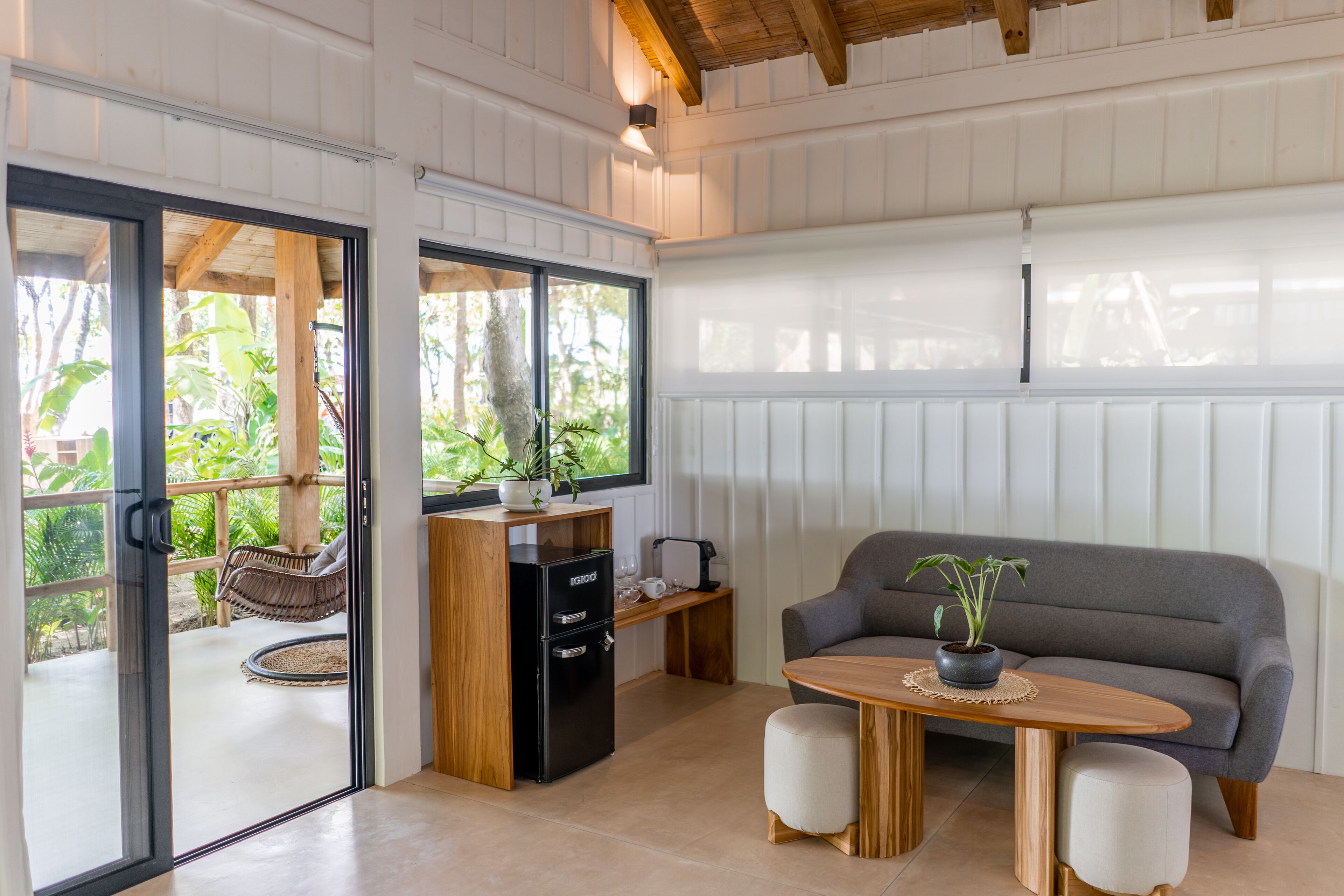 Un interior moderno con un sofá, una mesa con una planta y una pequeña zona de cocina con refrigerador y cafetera.
