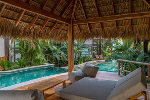 An indoor pool area with a thatched roof, wooden deck, and lounge chairs. - Blue Mist Hotel & Beach Club (Cóbano)