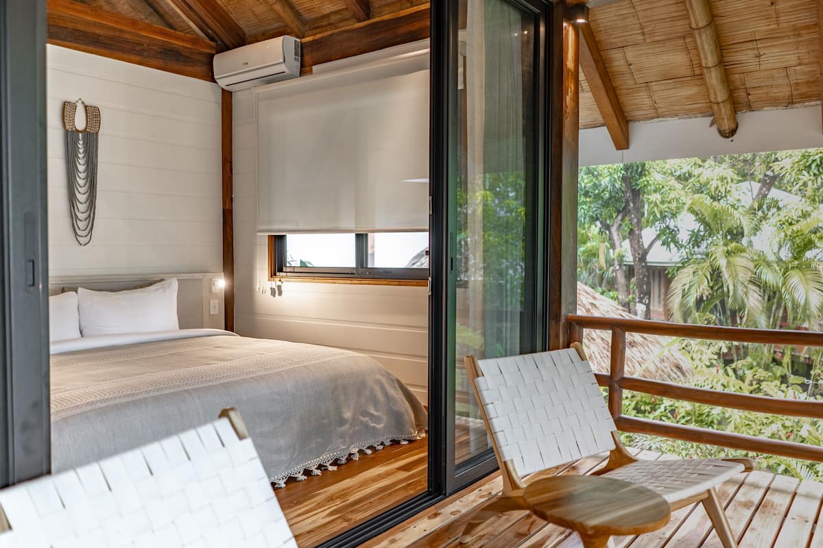 A bedroom with a bed, a window, and a view of greenery outside.