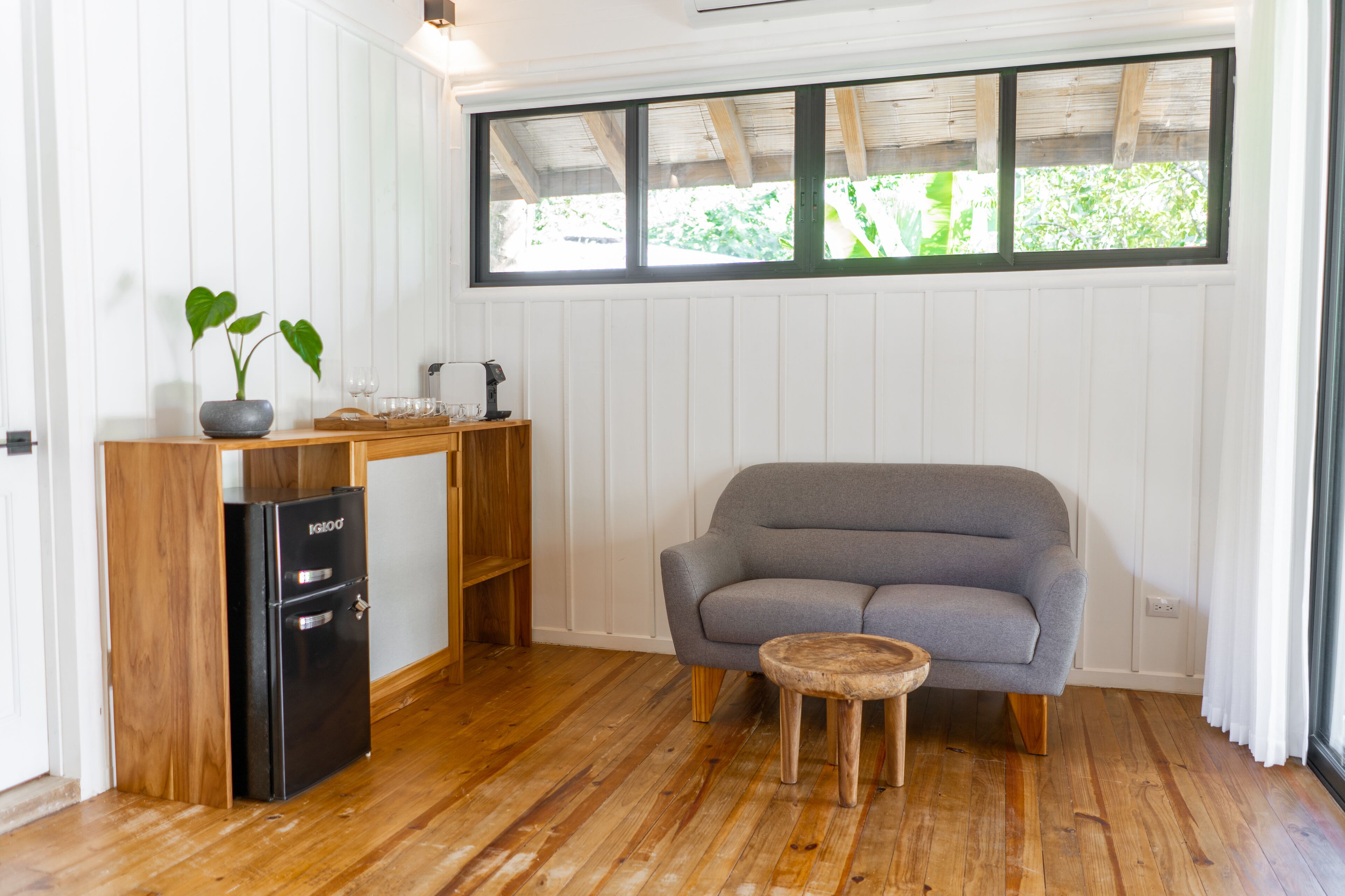 A compact room with a grey sofa, a small wooden table, a black refrigerator, and a potted plant.
