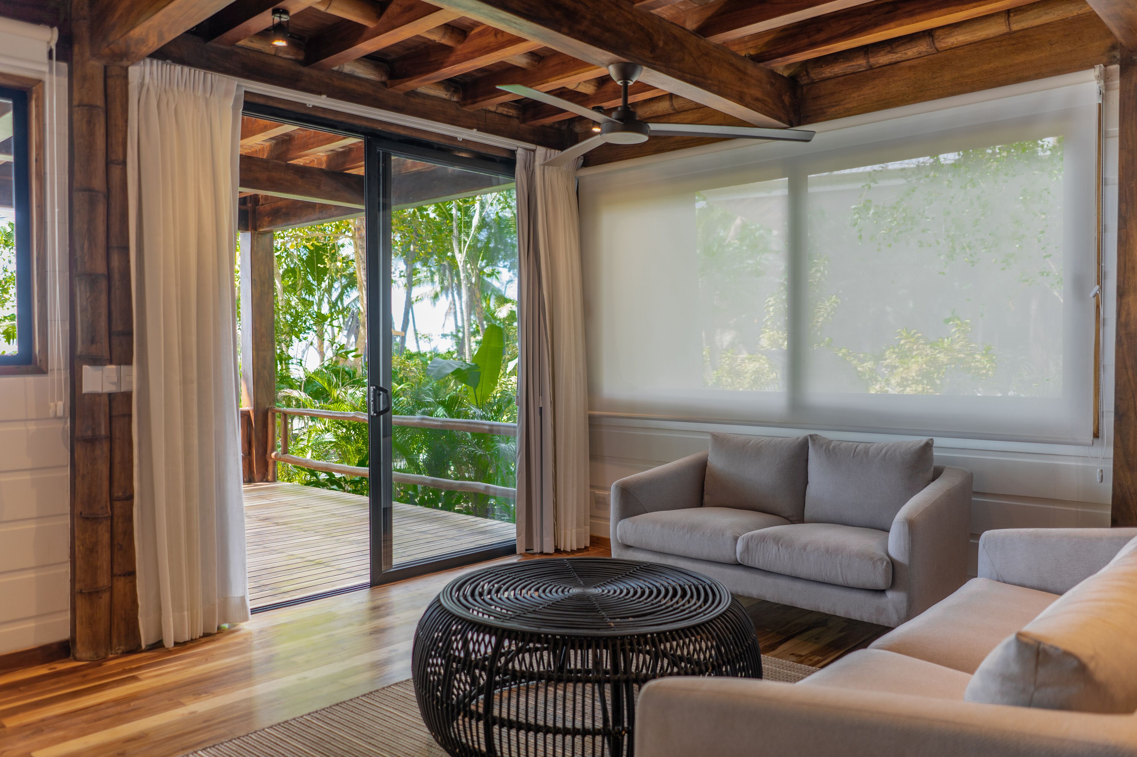 A modern living room with a sofa, a round black coffee table, and a large window with a view of greenery.