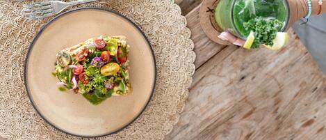 A plate of salad on a woven placemat, a fork and knife on a wooden table, and a glass of green drink with a lemon slice.