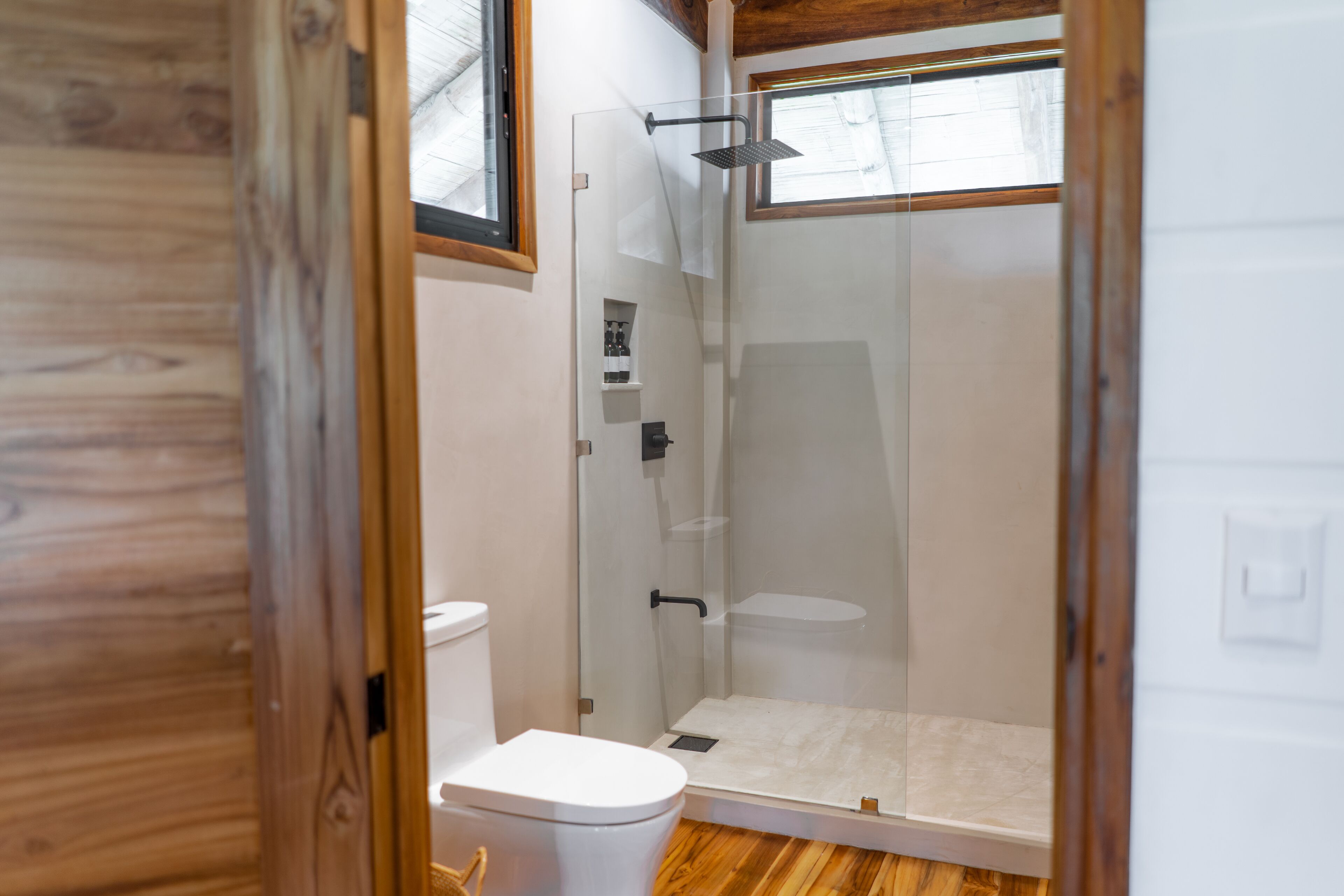 A modern bathroom with a glass-enclosed shower, a toilet, and a wooden floor.
