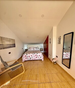 A bedroom with a bed, a chair, a mirror, and a small table with flowers.
