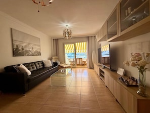 A living room with a sofa, TV, chess set, and a view to the outside.