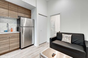 Una cocina compacta con refrigerador de acero inoxidable, armarios de madera, un sofá de cuero negro y una pequeña mesa.