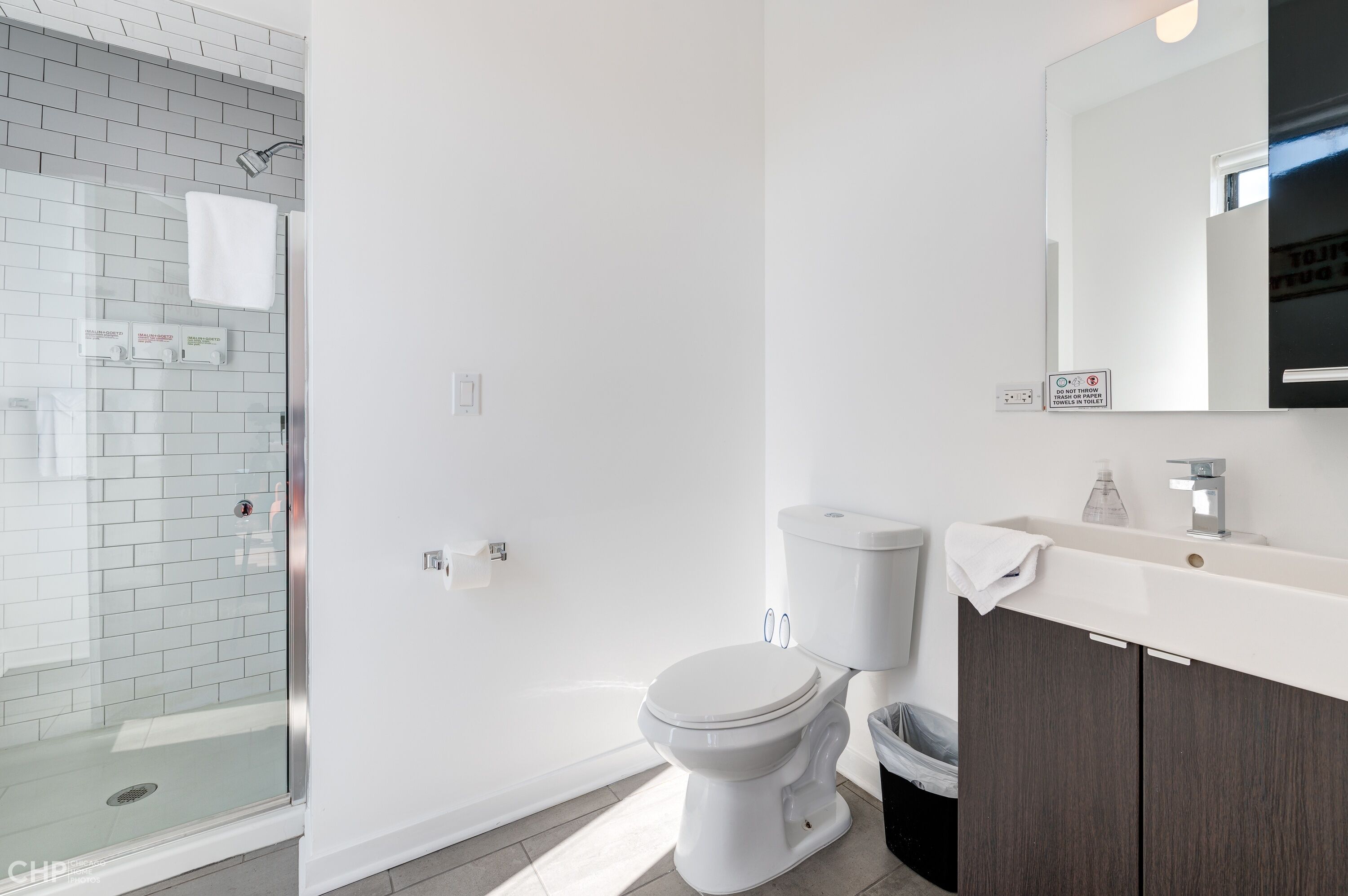 Un baño moderno con cabina de ducha de vidrio, inodoro blanco y tocador con espejo.