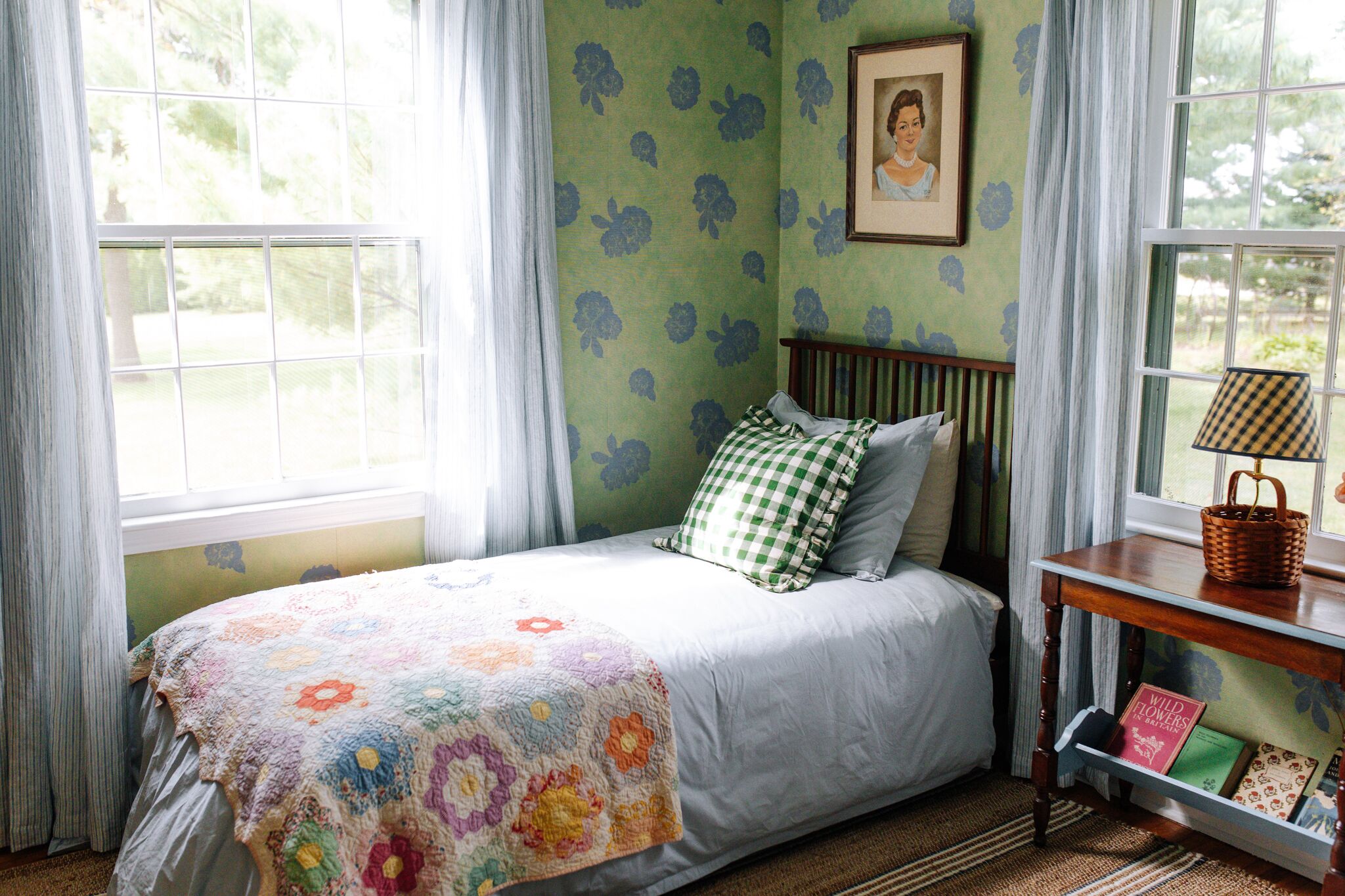 A bedroom with a bed, a bedside table with a lamp, a framed picture on the wall, and a window with curtains.
