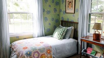 A bedroom with a bed, a bedside table with a lamp, a framed picture on the wall, and a window with curtains.
