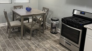 A kitchen with a dining table, chairs, a stove, and a trash can. - Beautiful Home (Riverdale)