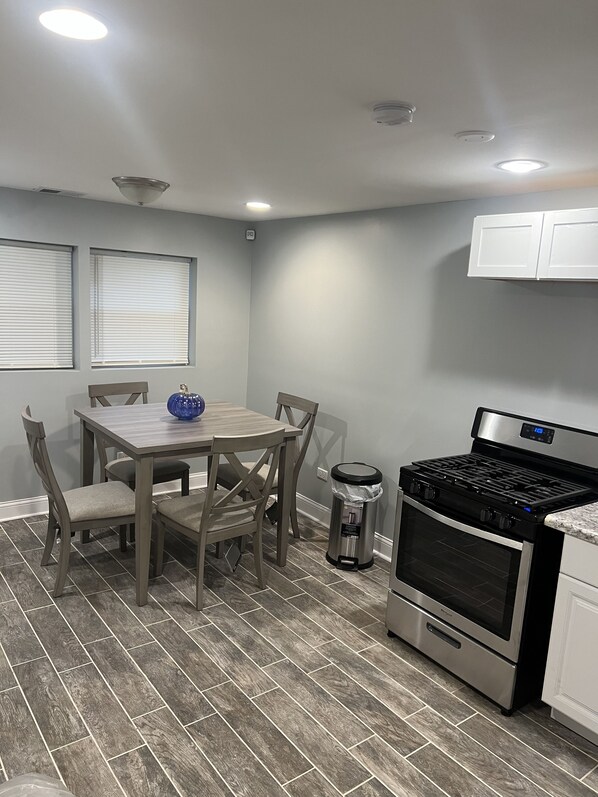 A kitchen with a dining table, chairs, a stove, and a trash can.
