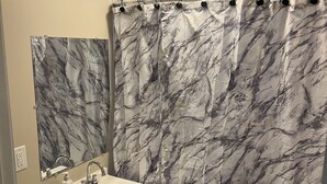 A bathroom with a marble-patterned shower curtain, a sink with a mirror above it, and a toilet. - Beautiful Home (Riverdale)