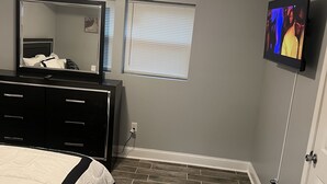 A bedroom with a bed, a dresser, a mirror, a television, and a window with blinds. - Beautiful Home (Riverdale)