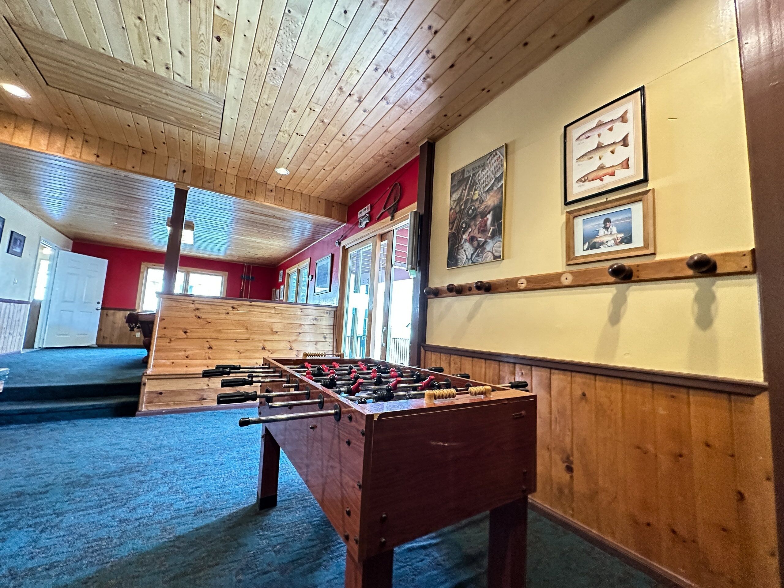 A room with a wooden ceiling, a foosball table, and a red wall with framed pictures.