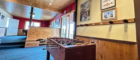 A room with a wooden ceiling, a foosball table, and a red wall with framed pictures.