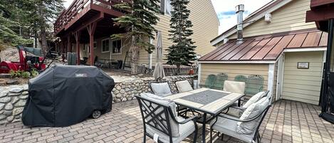 An outdoor patio with a table and chairs, a barbecue grill, and a stone wall.