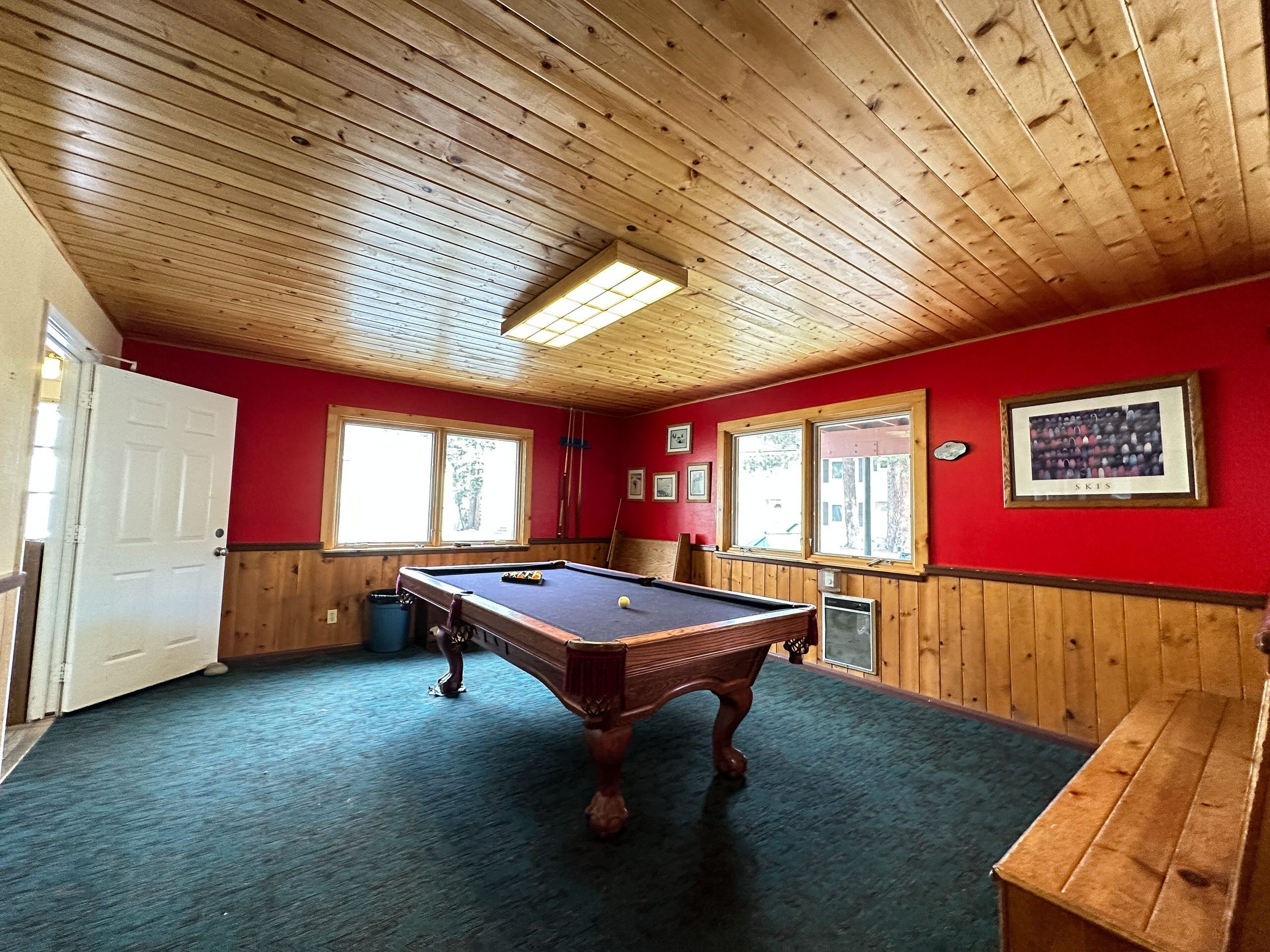 Een pooltafel in een ruimte met houten plafond en rode wanden, een deur en ramen.