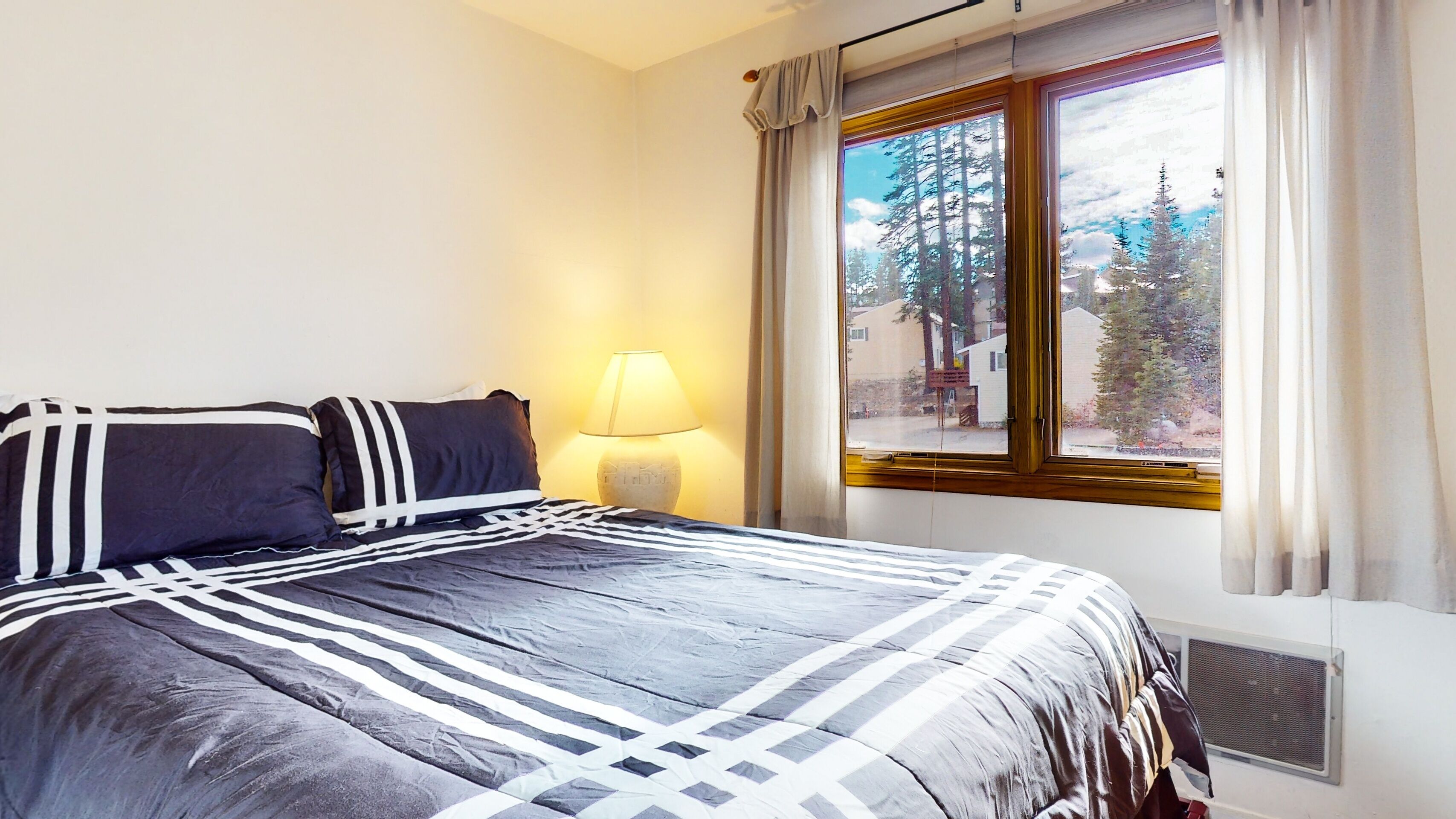Une chambre à coucher avec un lit, une lampe et une fenêtre donnant sur des arbres.