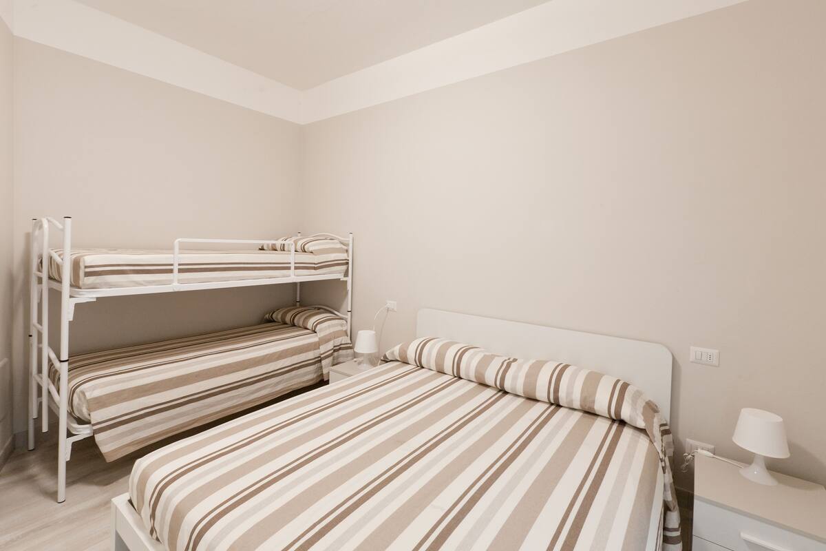 A bunk bed room with striped bedding and a bedside table with a lamp.