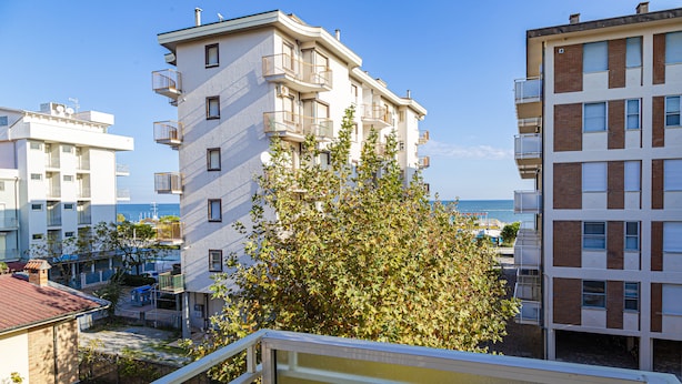Un edificio residencial de varios pisos con balcones, un jardín visible y una vista despejada del mar.