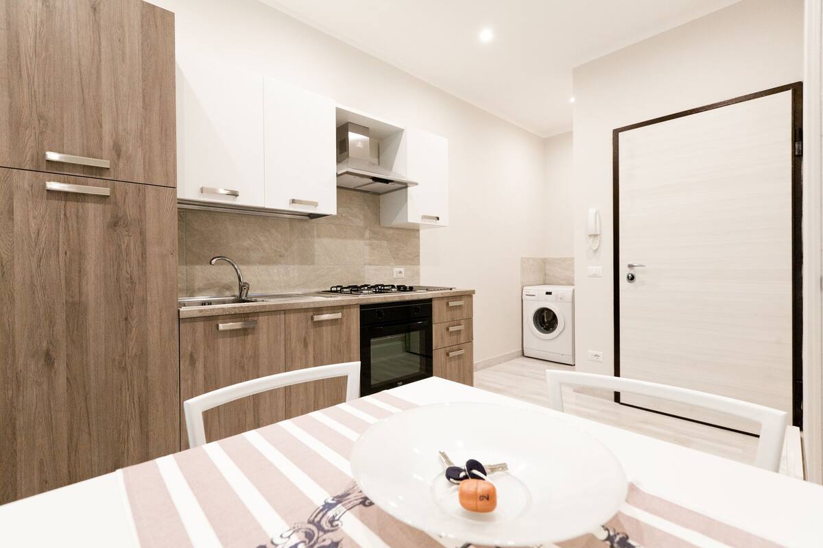 A compact kitchen with modern appliances, a dining area with a striped tablecloth, and a washing machine.
