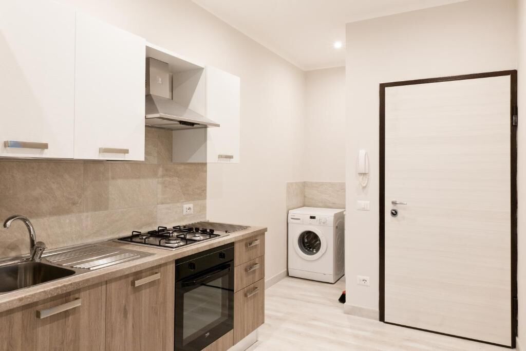 A compact kitchen with a gas stove, sink, and built-in oven. A washing machine is visible in the adjacent room.