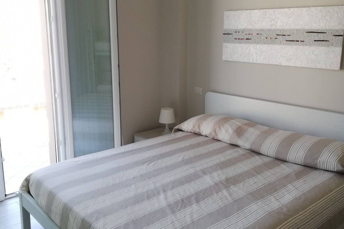 A bedroom with a bed, a nightstand, a lamp, and a sliding glass door leading to a balcony.