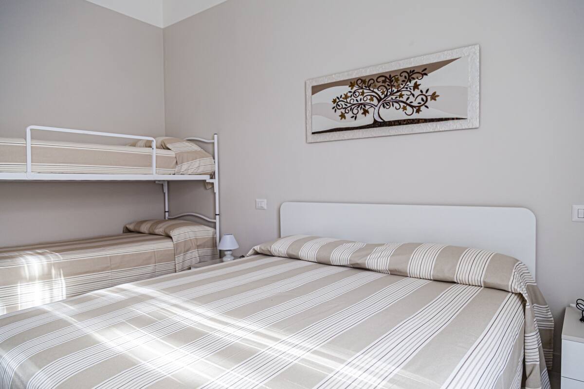 A room with two bunk beds, a bedside table with a lamp, and a wall-mounted artwork.
